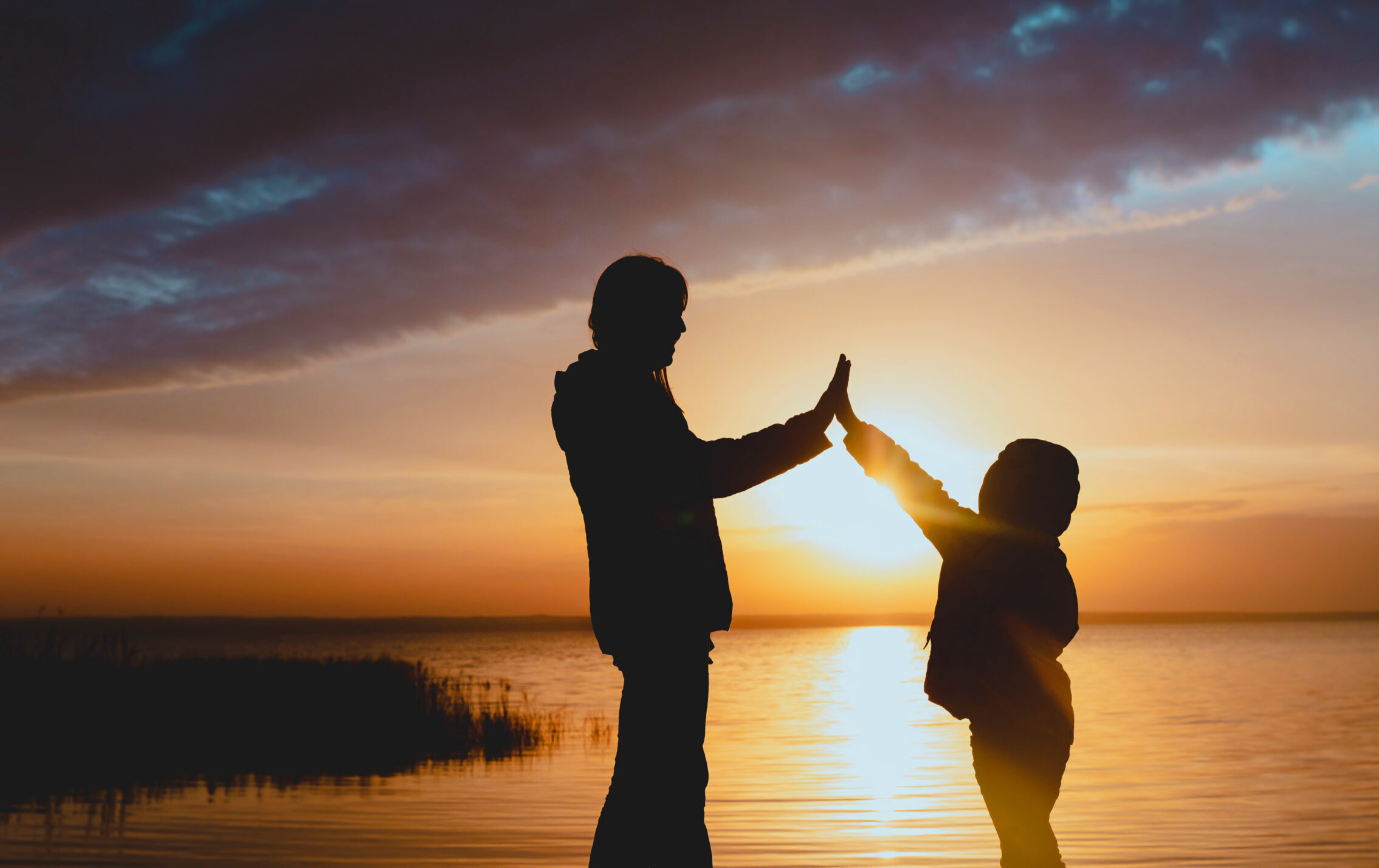 happy mother with daughter high five at sunset on lake