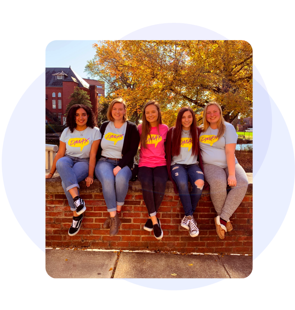 five girls sitting on a brick wall wearing DMAX shirts